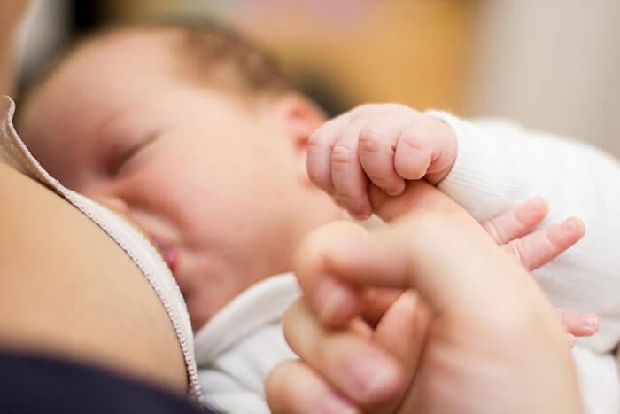 bir bebek annesinin parmağını sıkıca tutarak annesinin memesinden süt emmekte.