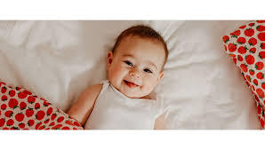  yatakta yatan bir bebek gülümseyerek bakıyor